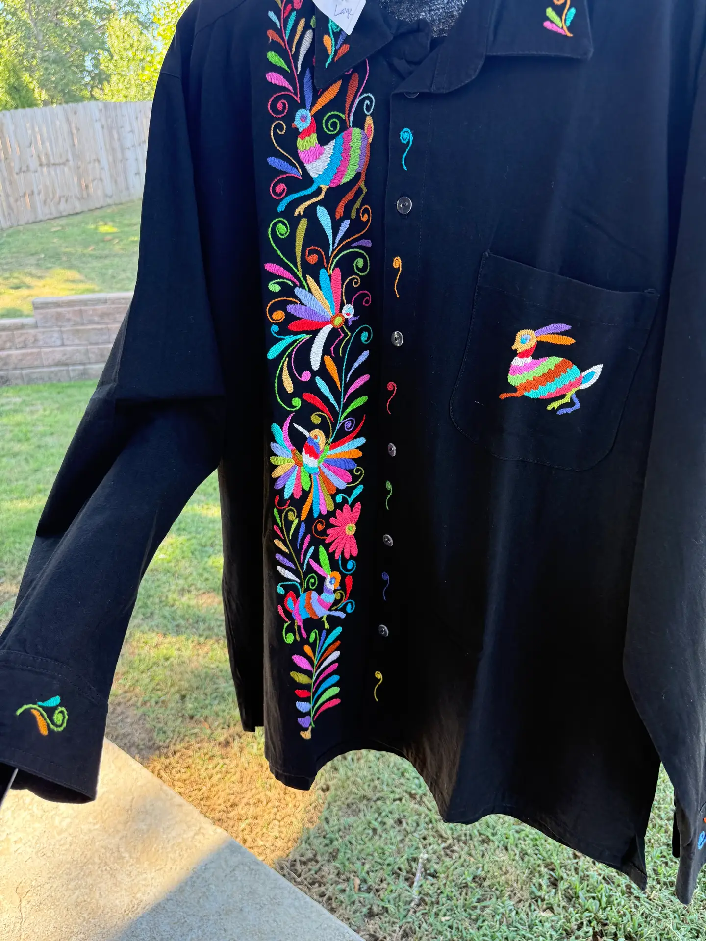 Front view of a black cotton men's shirt with pastel floral and hare Tenango embroidery.