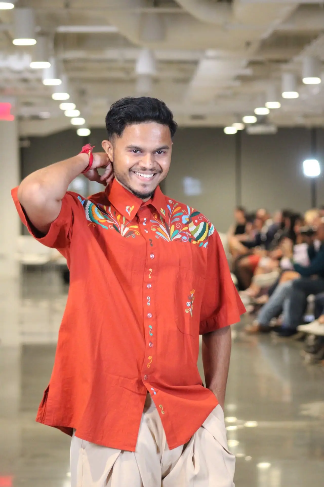 Man wearing a brick colored short-sleeve shirt with vibrant Tenango embroidery.