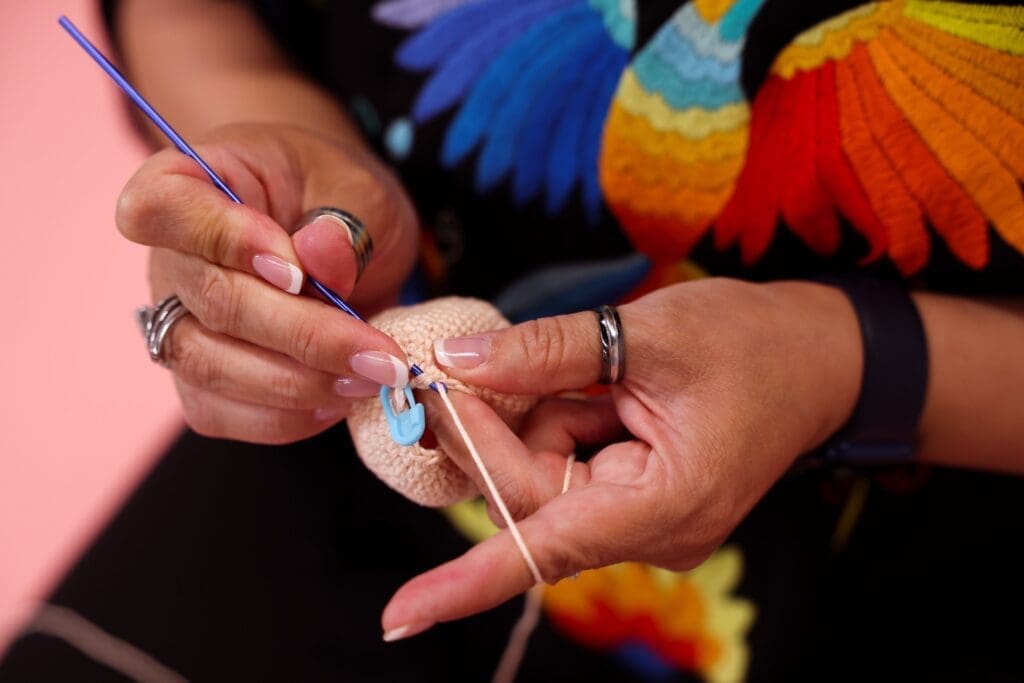 Photo of a woman working on an crochet project. The photo is a close up of her hands.